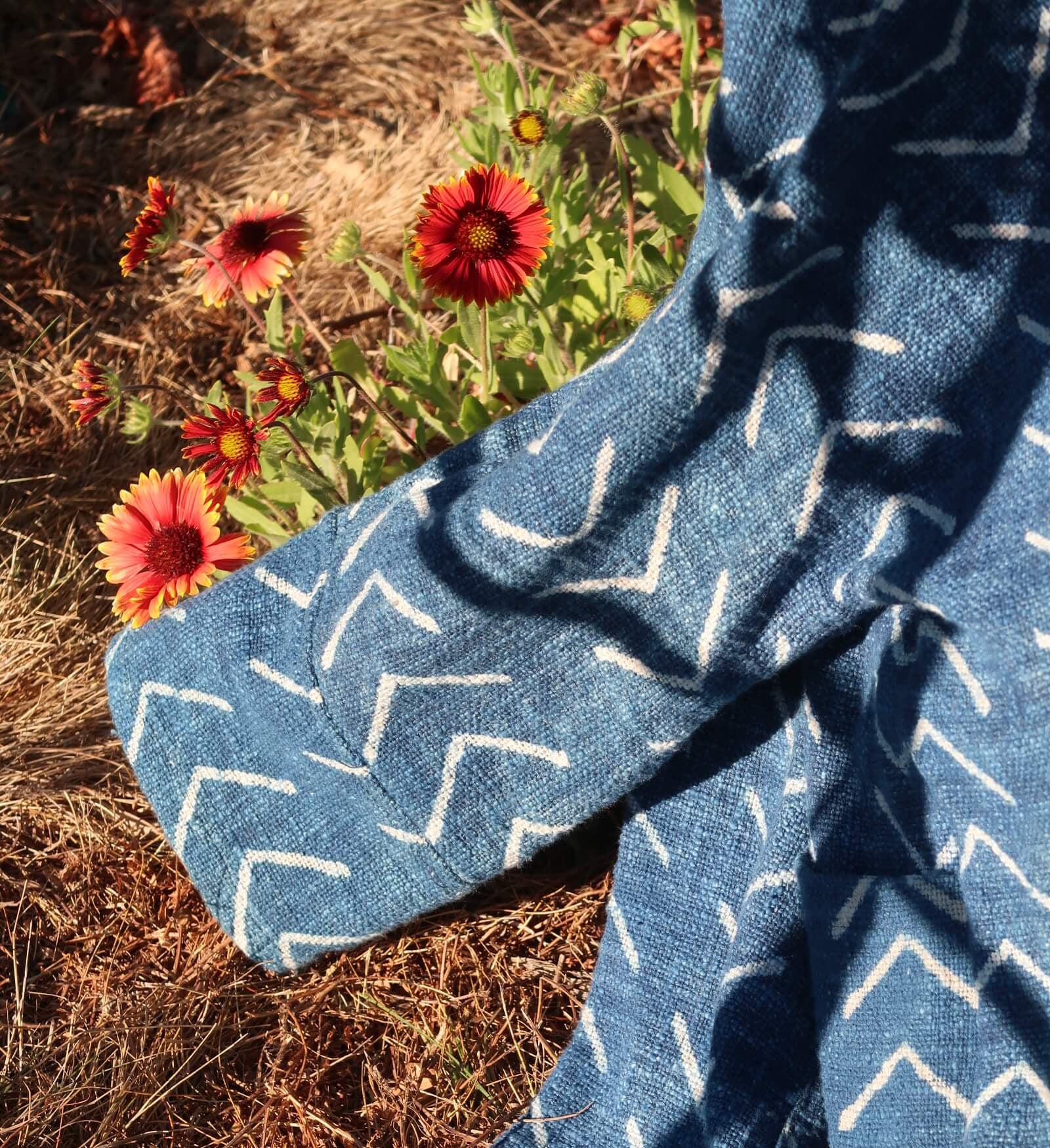 Blue fabric with white patterns draped over a natural setting with flowers and grass.